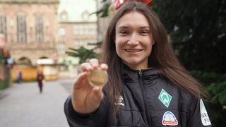 Werder-Stürmerin Sophie Weidauer hält strahlend auf dem Bremer Weihnachtsmarkt ihre Medaille für das "Tor des Monats" der ARD-Sportschau in die Kamera.