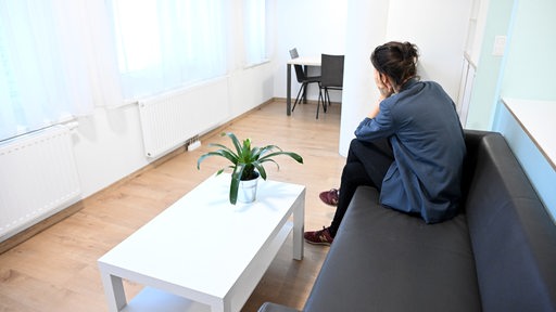 Eine Frau sitzt in einem Frauenhaus auf einem Sofa.