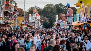 Besucher gehen zwischen Ständen und Fahrgeschäften auf dem 989. Freimarkt in Bremen. 