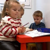 Kleine Kinder sitzen an einem roten Tisch.