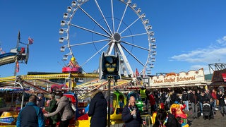 Das Riesenrad und verschiedene Fahrgeschäfte mit Besuchern auf dem Bremer Freimarkt bei strahlendem Wetter.