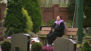 Die Bremer Pastorin Hannah Detken sitzt auf dem Friedhof auf einer Bank zwischen den Gräbern.