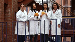 Vier Frauen in weißem Kittel stehen hinter einem Geländer, zwei halten etwas in den Händen.