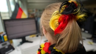 Eine Frau mit Deutschland-Farben im Haar schaut auf ihren Bildschirm.