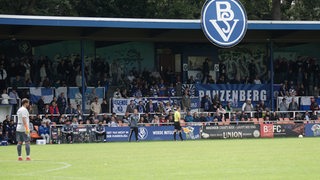 Malte Seemann steht im Tor, die Fans verfolgen das Spiel von der Tribüne.