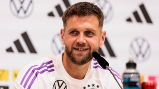 Niclas Füllkrug sitzt in einem T-Shirt der deutschen Nationalmannschaft auf dem Podium bei einer Pressekonferenz.