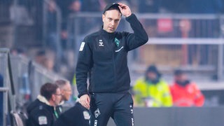 Werder-Trainer Ole Werner steht beim Pokalspiel in Bielefeld konsterniert an der Seitenlinie und zieht sich die schwarze Kappe wieder auf den Kopf.