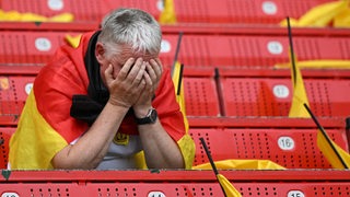 Ein deutscher Fußball-Fan vergräbt enttäuscht sein Gesicht in seinen Händen nach dem Aus der deutschen Elf bei der EM.