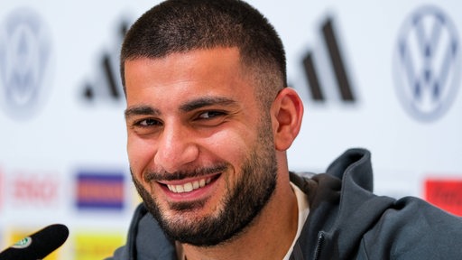 Der deutsche Nationalspieler Deniz Undav grinst schelmisch auf dem Podium einer Pressekonferenz während der EM.