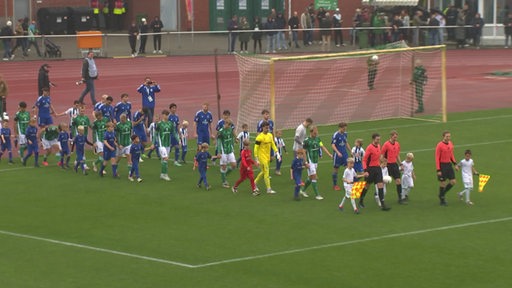 Zwei Fußballmannschaften laufen in das Stadion ein.