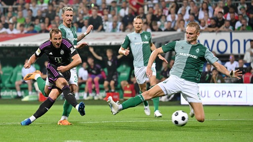 Harry Kane von Bayern München schießt aufs Tor. Amos Pieper versucht den Ball per Grätsche abzufangen.
