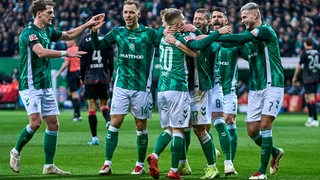 Mehrere Werder-Spieler kommen im Spiel gegen Union Berlin auf dem Spielfeld zusammen, um mit Marco Grüll dessen Tor zu feiern.