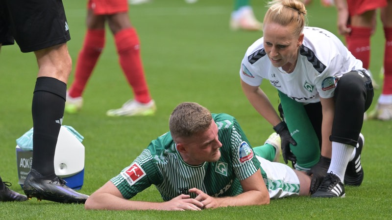 Werder-Stürmer Marvin Ducksch liegt während des Spiels gegen Mainz bäuchlings auf dem Rasen und wird von der Physiotherapeutin am Bein behandelt.