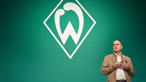 Werder-Geschäftsführer Klaus Filbry auf dem Podium vor der großen Werder-Raute an der Wand bei der Mitgliederversammlung.