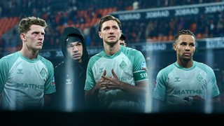 Die Werder-Profis Jens Stage, Justin Njinmah, Niklas Stark und Felix Agu stehen in Freiburg ernüchtert vor dem Gästefanblock.