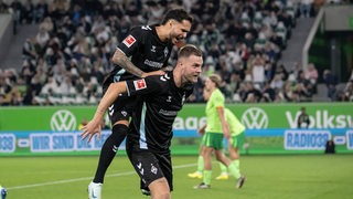 Das Foto zeigt zwei Fußballspieler, der eine springt jubelnd auf den Rücken des anderen.