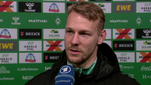 Werder-Torschütze Marco Grüll steht nach dem Spiel vor einer Werbewand beim Interview.