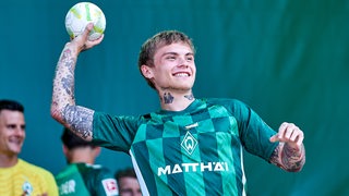 Werder-Spieler Isak Hansen-Aaröen wirft bei Tag der Fans strahlend einen Ball von der Bühne ins Publikum.