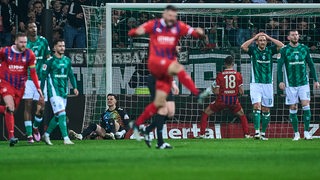 Werder-Spieler schauen frustriert nach einem Gegentor, während sich die Heidenheimer Spieler freuen.