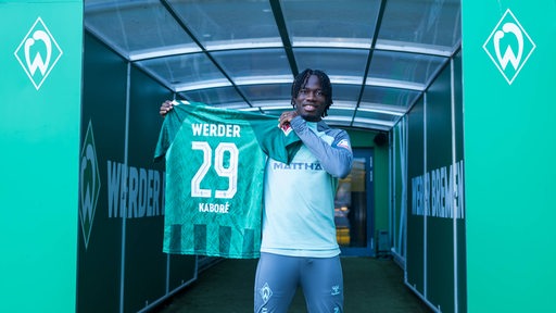 Issa Kaboré steht im Spielertunnel des Weser-Stadions und präsentiert sein Trikot mit der Rückennummer 29.