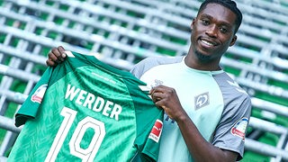 Werder-Neuzugang Derrick Köhn hält bei seiner Vorstellung sein Trikot mit der Rückennummer 19 hoch.