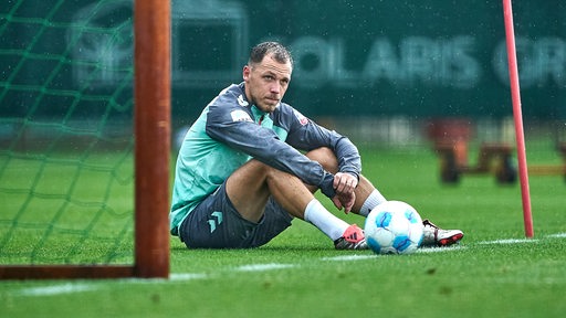 Werders Fußballprofi Senne Lynen sitzt mit angewinkelten Beinen frustriert während des Trainings im Tor.