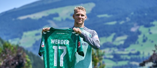 Marco Grüll hält ein Werder-Trikot mit der Nummer 17 hoch.