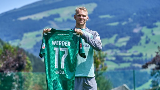 Marco Grüll hält ein Werder-Trikot mit der Nummer 17 hoch.