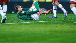 Werder-Stürmer Justin Njinmah liegt mit Schmerzen auf dem Rasen und hält sich den rechten Knöchel.