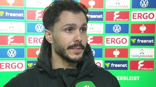 Werder-Profi Leonardo Bittencourt steht nach dem Pokal-Aus in Bielefeld vor einer Werbewand beim Interview.