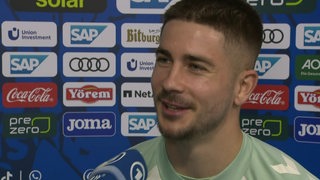 Werder-Profi Romano Schmid steht lächelnd nach dem Sieg gegen Hoffenheim beim Interview vor einer Werbewand.