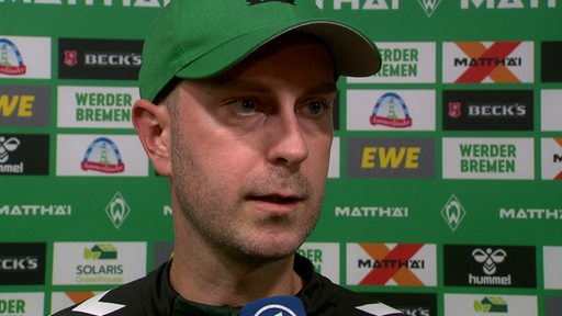 Werder-Trainer Ole Werner beim Interview nach dem Spiel vor einer Werbewand.