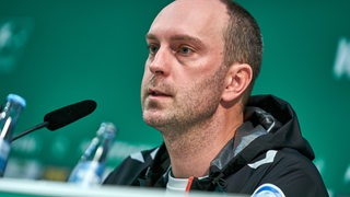 Werder-Trainer Ole Werner sitzt auf dem Podium einer Pressekonferenz.