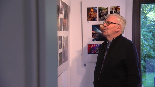 Ein älterer Mann schaut auf eine Wand voller Fotos.