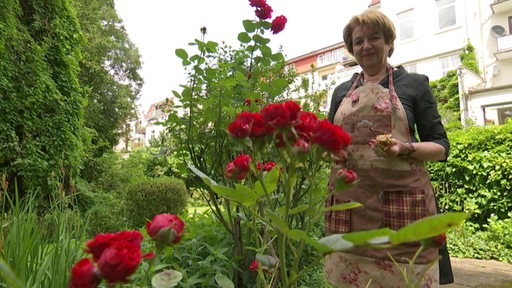 Eine Frau steht in einem Garten mit rot blühenden Rosen.