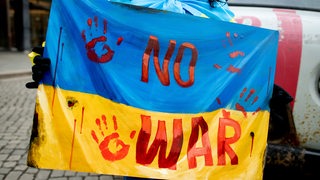 Auf dem Marktplatz in Bremen hält eine Frau ein Plakat mit in den Farben der Ukraine mit der Aufschrift "No War"