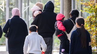 Eine Familie mit kleinen Kindern geht eine Straße entlang, sie tragen Kapuzen und dicke Pullover.