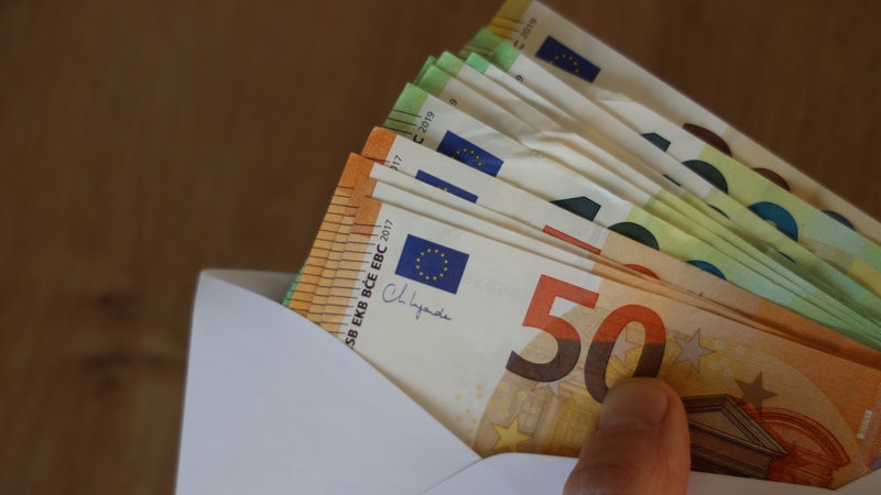 Eine Hand hält einen Briefumschlag voller 50- und 100-Euro-Scheine