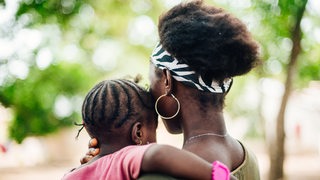 Rückenansicht einer afrikanischen jungen Frau mit einem Kind auf dem Arm.