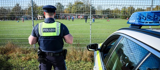 Ein Polizeibeamter beobachtet ein Amateur-Fußballspiel hinter einem Zaun.