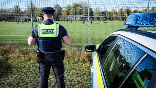 Ein Polizeibeamter beobachtet ein Amateur-Fußballspiel hinter einem Zaun.