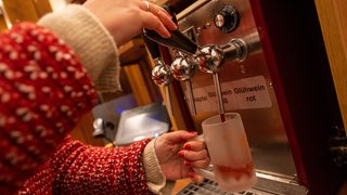 Eine Verkäuferin schenkt Glühwein in eine Tasse ein. 