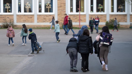 Schüler gehen über den Schulhof zum Schulgebäude.