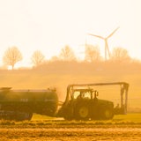 Ein Trecker fährt über ein Feld und düngt, während die Sonne aufgeht.