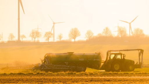 Ein Trecker fährt über ein Feld und düngt, während die Sonne aufgeht.