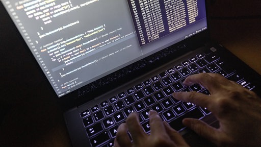 Quellcode eines Webservers sowie die Windows-Eingabeaufforderung sind einem Laptop im Dunkeln zu sehen. Hände tippen auf der Tatstatur des Laptops.