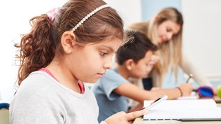 Mädchen schaut auf ein Smartphone im Unterricht einer Grundschule