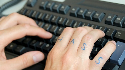 Hände über einer Computertastatur, auf einer Hand steht das Wort "Hass" auf den Fingern. (Symbolbild)