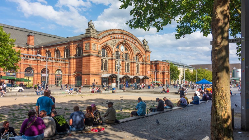 Menschen sitzen mit Getränken auf den Bürgersteigen vor dem Bremer Hauptbahnhof