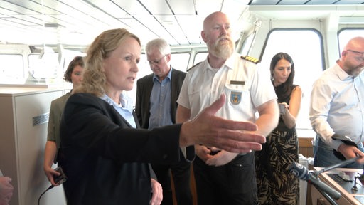 Die Umweltministerin Lehmke steht mit dem Kapitän in der Kommandobrücke eines Schiffes.